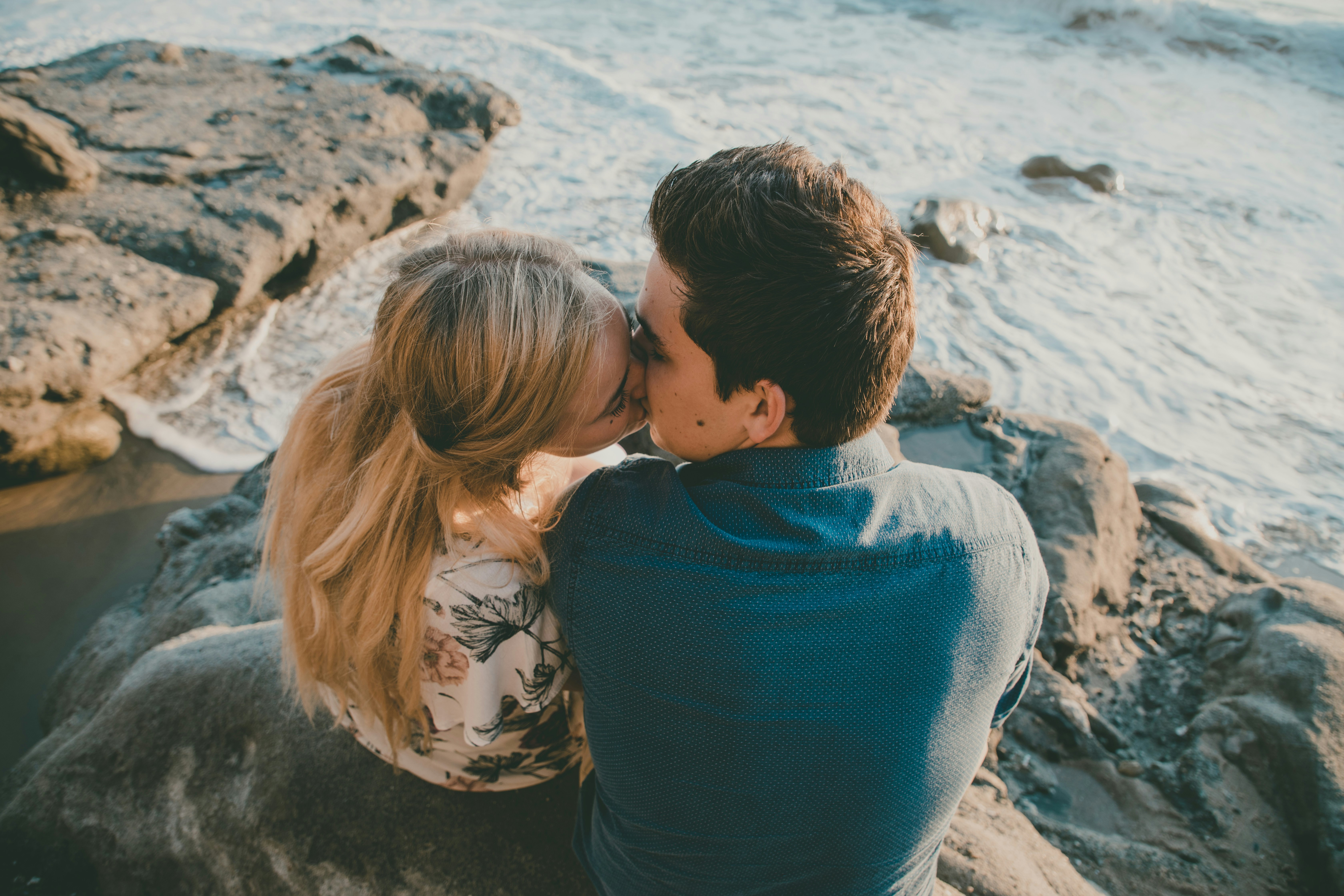 couple kissing white sitting on rock at the beach